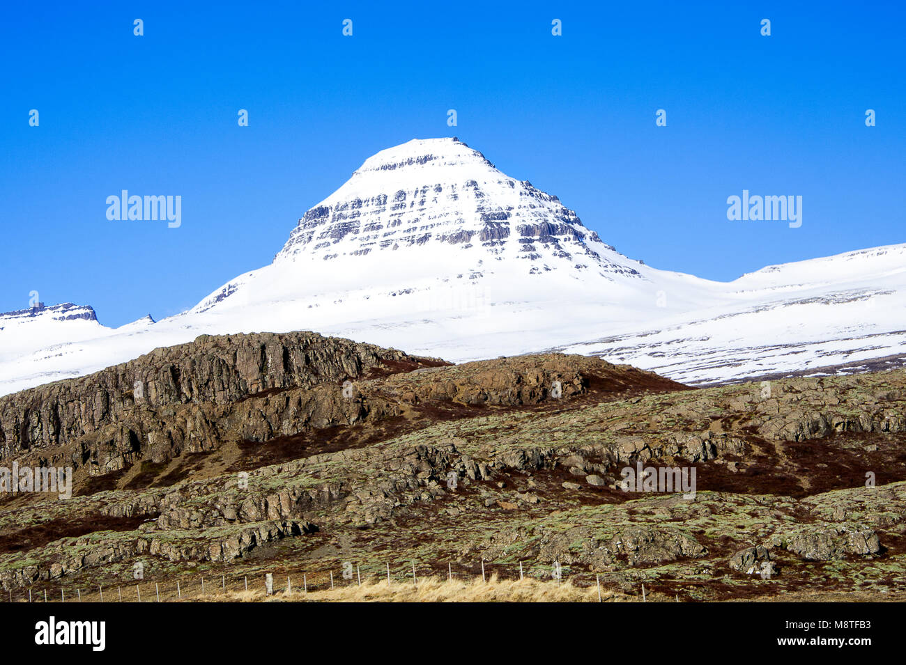 Contraste frappant de pics couverts de neige, blanc et coloré, strié, formations rocheuses à l'avant-plan. Beaux Fjords de l'Est de l'Islande, paysage Banque D'Images