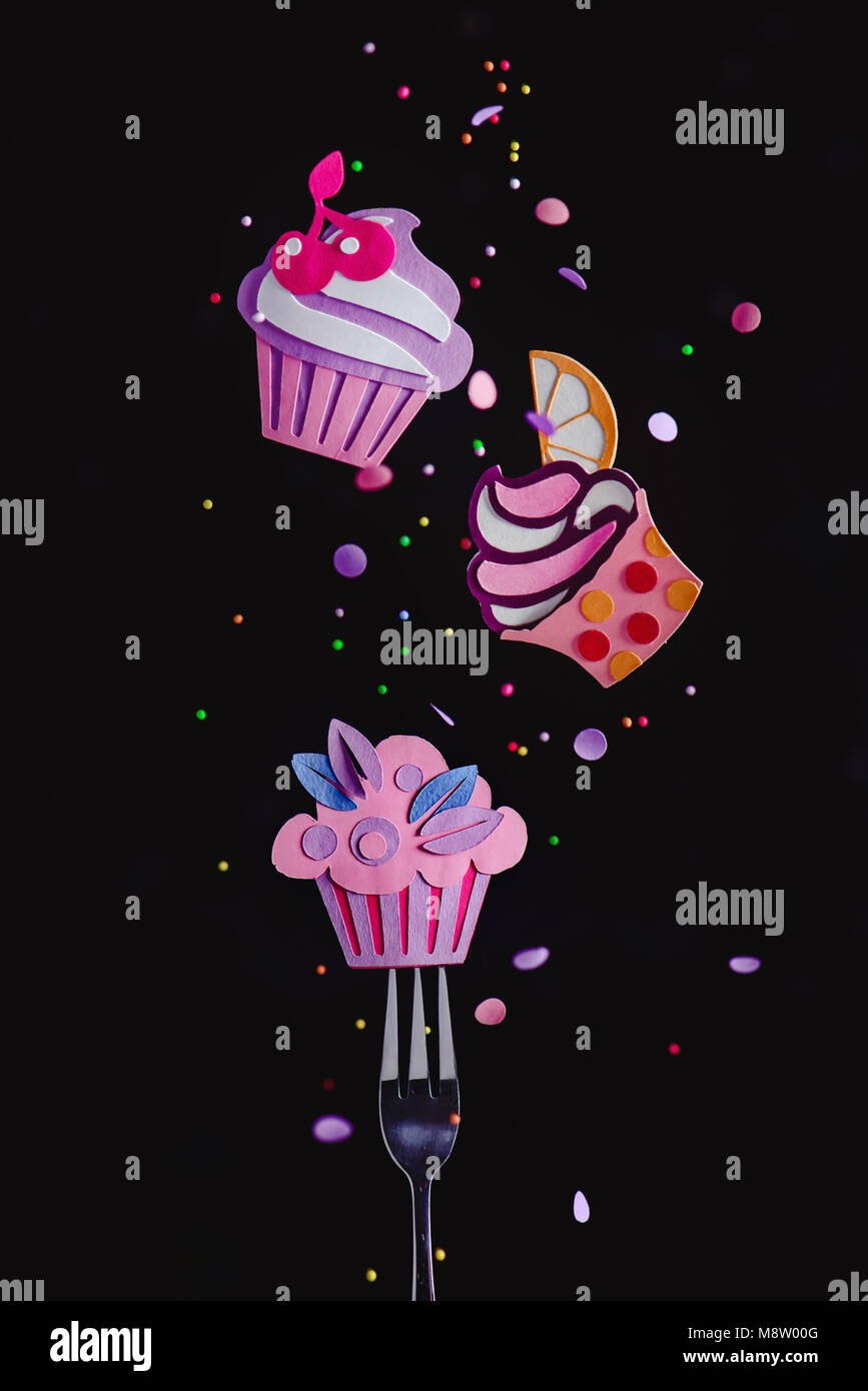 Cupcakes colorés volant au-dessus d'une fourchette à dessert de confettis et paillettes. Traiteur concept avec copie espace. La photographie d'action alimentaire papercraft. Banque D'Images