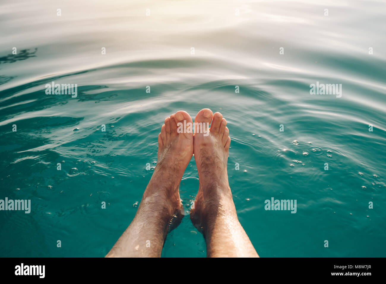 Les pieds mâles dans une piscine extérieure. L'eau de la piscine rafraîchissante Man enjoying coucher du soleil en été. Activités du week-end et vacances. Banque D'Images