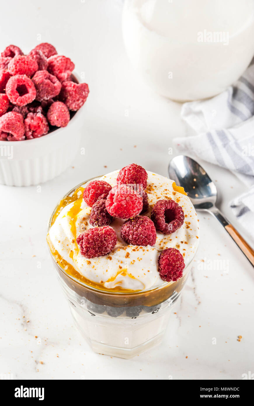 Un petit-déjeuner sain, la semoule au lait d'avoine dans du verre avec du lait, de la crème, de caramel et de fruits rouges, table en marbre blanc copy space Banque D'Images