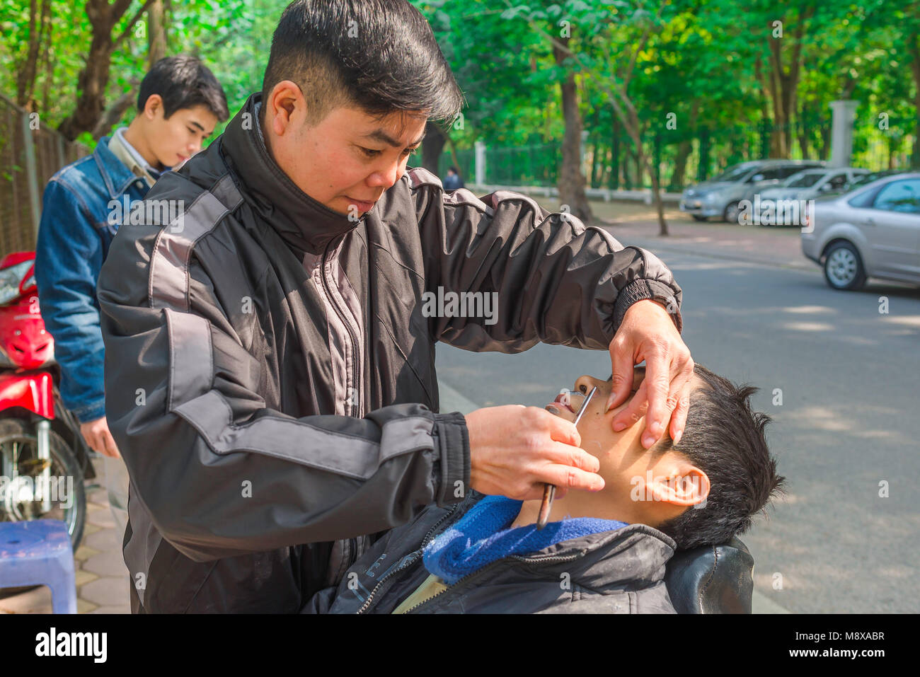 Barber Shaving man Street, un barbier de bord de route rasse un client près de West Lake à Hanoi, Vietnam. Banque D'Images