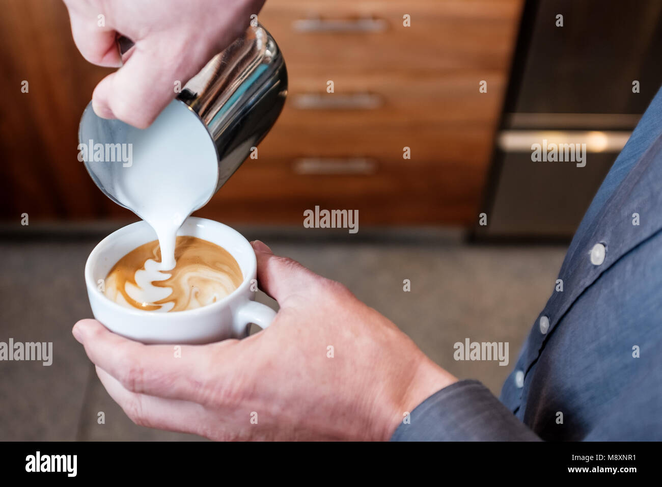 Verser le lait à la vapeur barista professionnel en acier inoxydable tumbler en rendant la tasse de café latte art sur cappuccino Banque D'Images