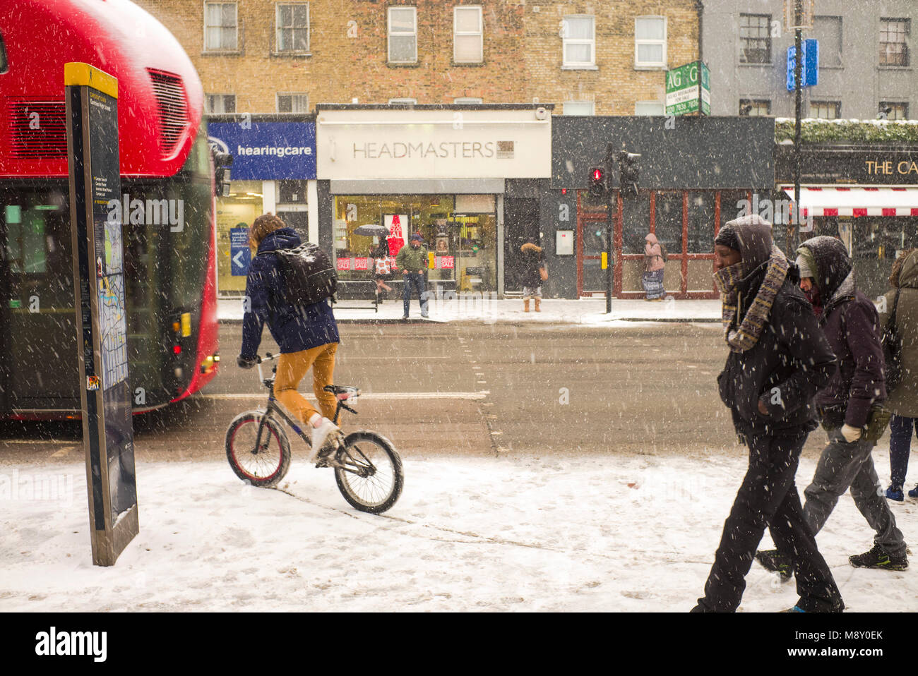Équitation à travers cycliste rue couverte de neige après London bus rouge Banque D'Images