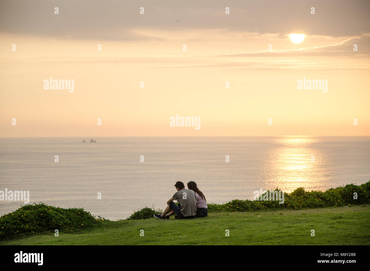 Un couple assis en face de la mer en admirant le coucher du soleil Banque D'Images