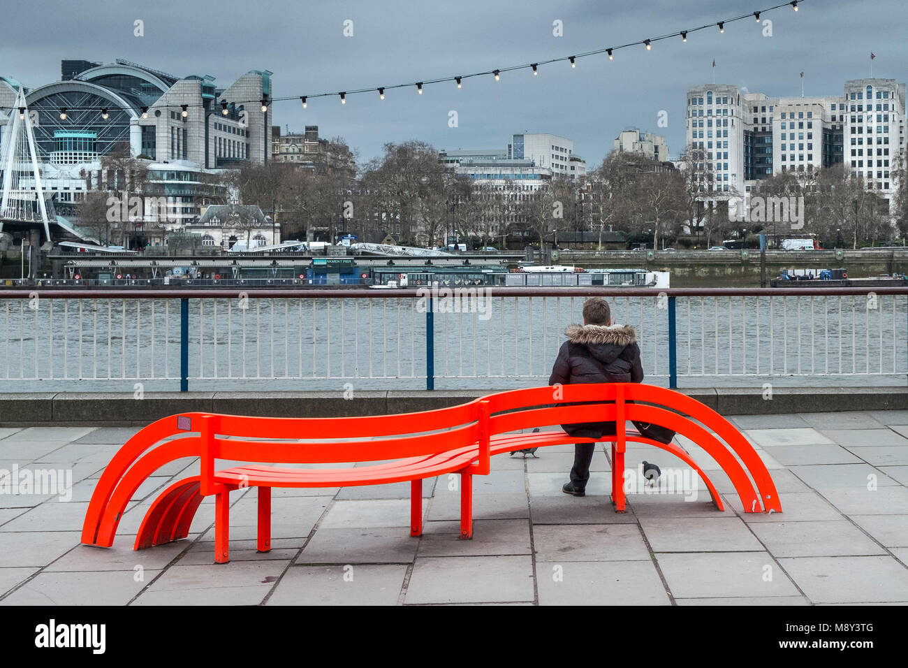 Une personne assise sur un banc de couleur vive sur la rive sud de Londres. Banque D'Images