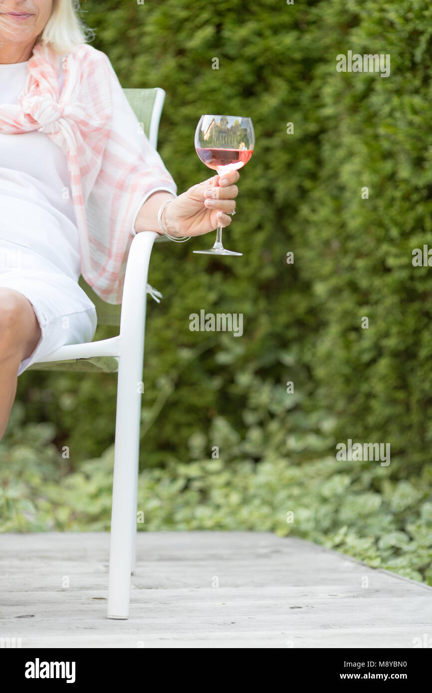 Une femme tenant un verre de vin rose sur un patio extérieur avec un fond vert Banque D'Images
