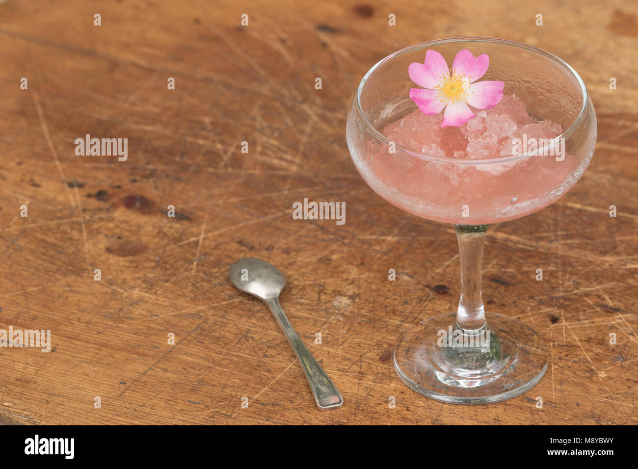 Vin rose congelé dans un verre avec une cuillère à dessert et pétales de rose biologique Banque D'Images