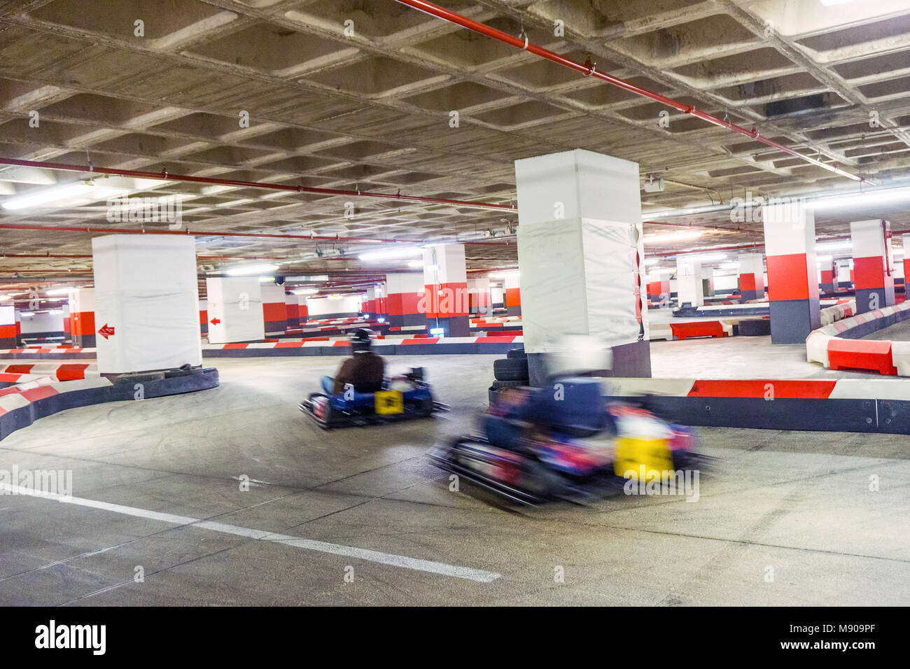 Deux personnes course sur piste de karting intérieur situé dans un parking souterrain Banque D'Images