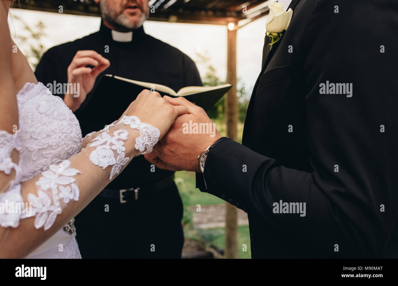 Close up de jeunes mariés qui se tiennent la main pendant la cérémonie de mariage en plein air. Prêtre l'exécution d'une cérémonie de mariage pour un couple à l'extérieur. Banque D'Images Close up de jeunes mariés qui se tiennent la main pendant la cérémonie de mariage en plein air. Prêtre l'exécution d'une cérémonie de mariage pour un couple à l'extérieur. Banque D'Images