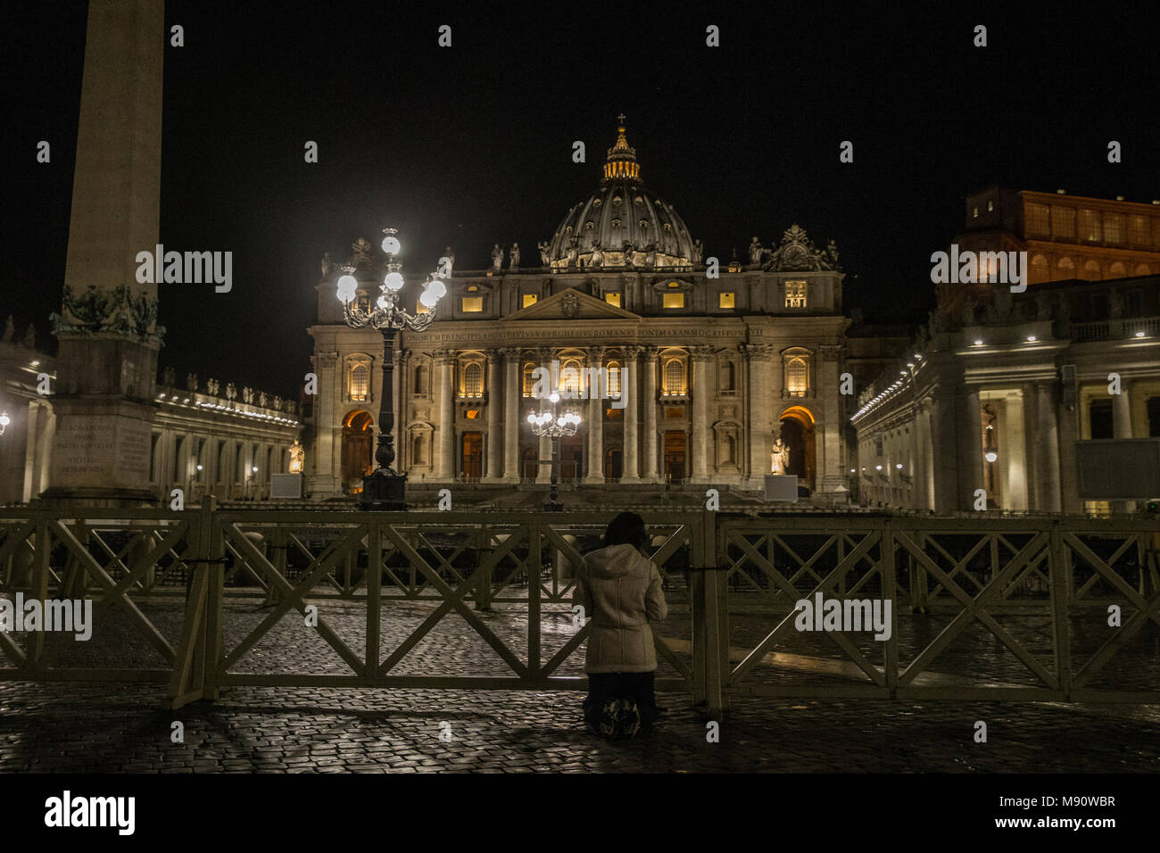 Femme agenouillée priant à l'extérieur de la basilique Saint Pierre la nuit. Rome, Italie. Banque D'Images