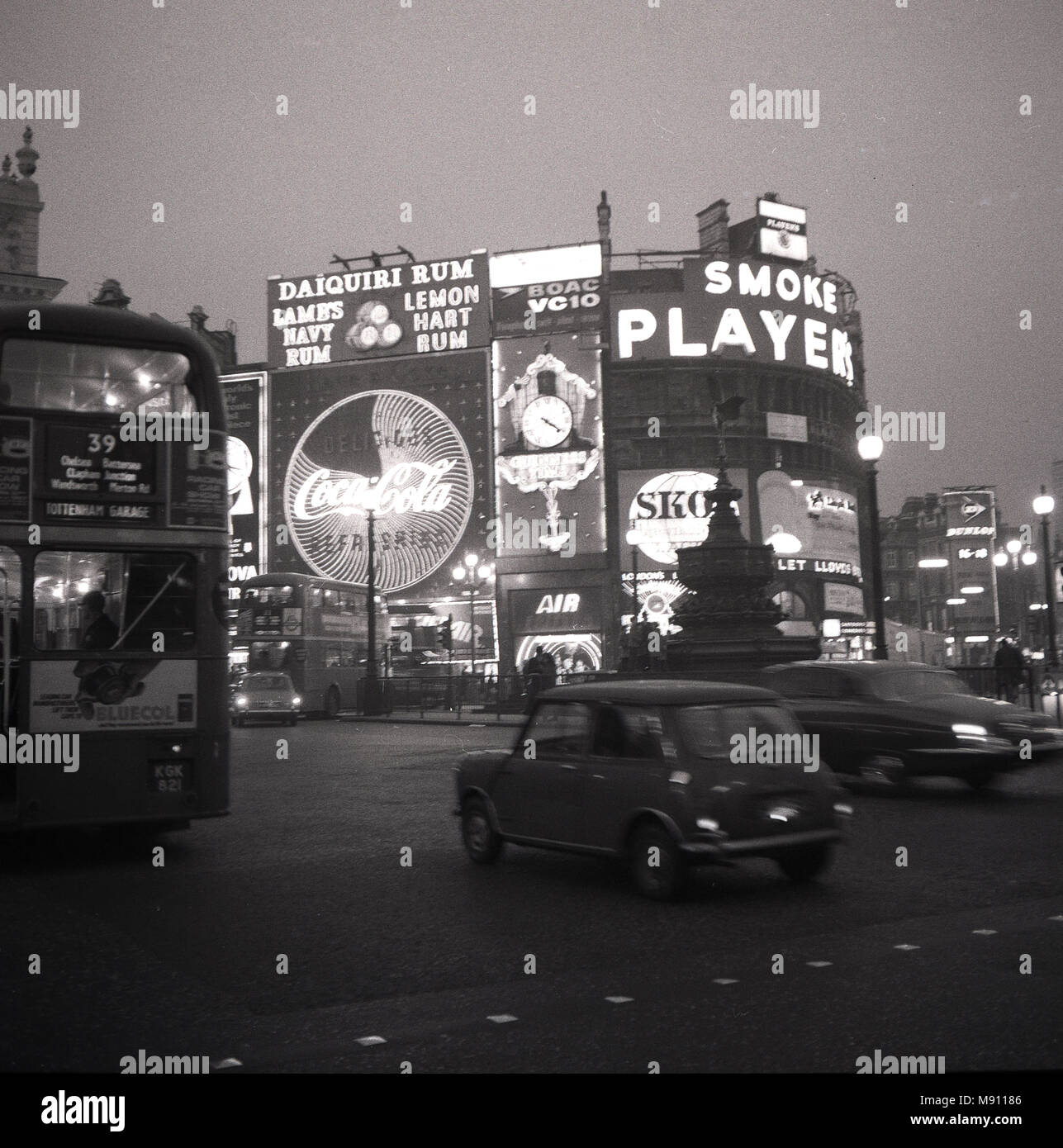 Années 1960, photo historique montrant Londres Piccadilly Circus à temps le soir avec des véhicules et de la célèbre lumière néon les panneaux publicitaires pour des marques telles que comme "acteurs cigarettes' et 'coca-cola'. Banque D'Images