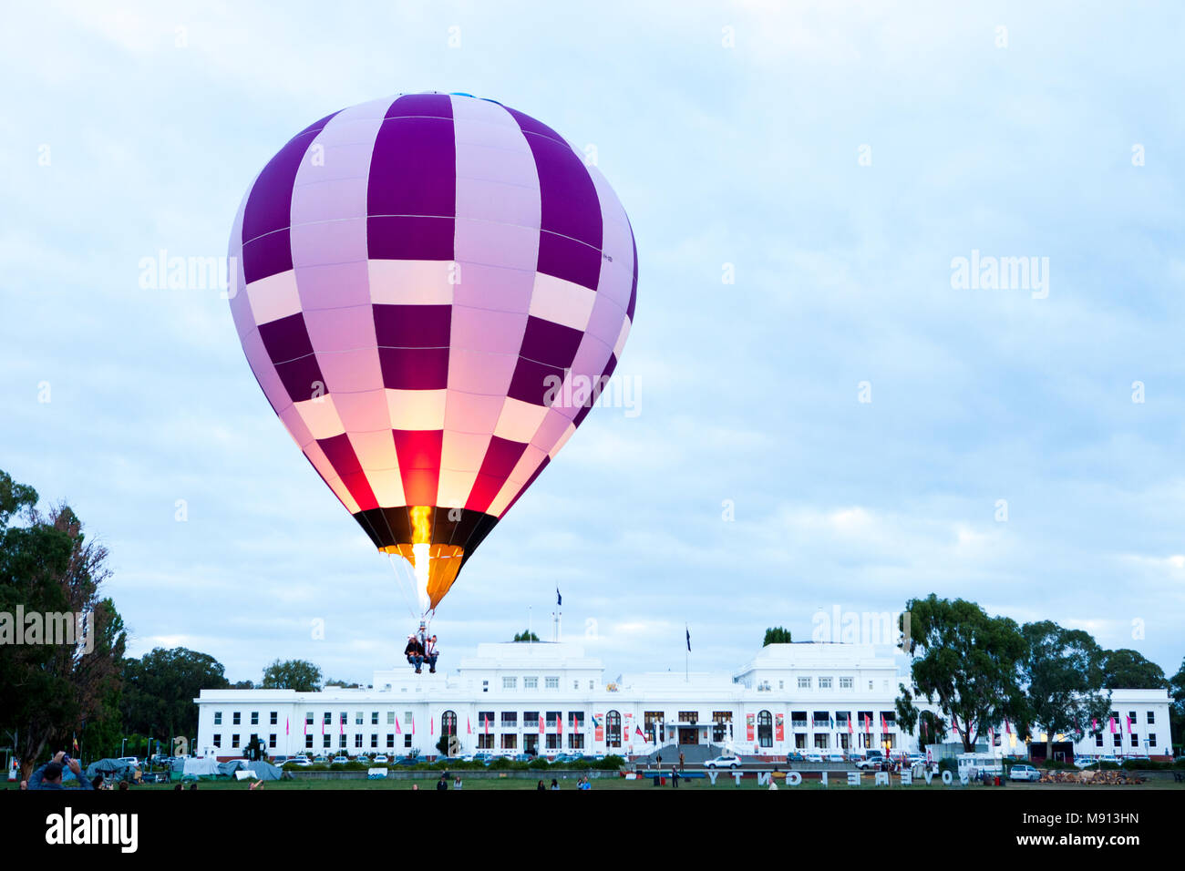 Un ballon à air chaud coloré violet et blanc injecte du feu et de l'air chaud dans le ballon lorsqu'il passe devant l'Old Parliament House, Canberra Banque D'Images