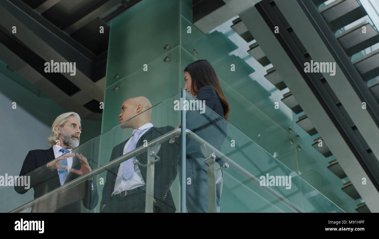 Trois cadres de la société multinationale standing au deuxième étage de l'immeuble de bureaux modernes de discuter affaires. Banque D'Images