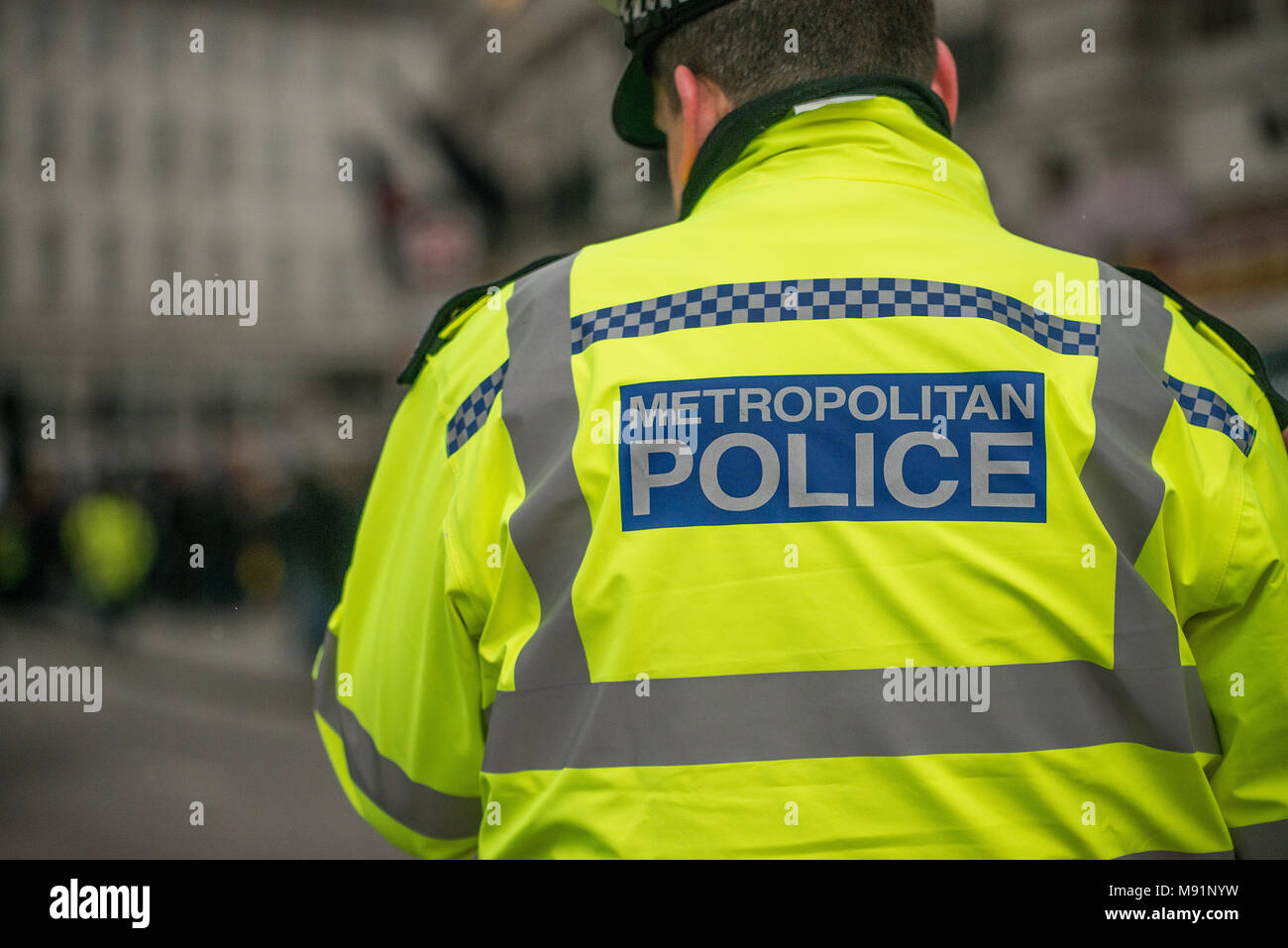 Agent de police avec son dos à la caméra avec la Police métropolitaine signe sur sa veste réfléchissante jaune.. Banque D'Images