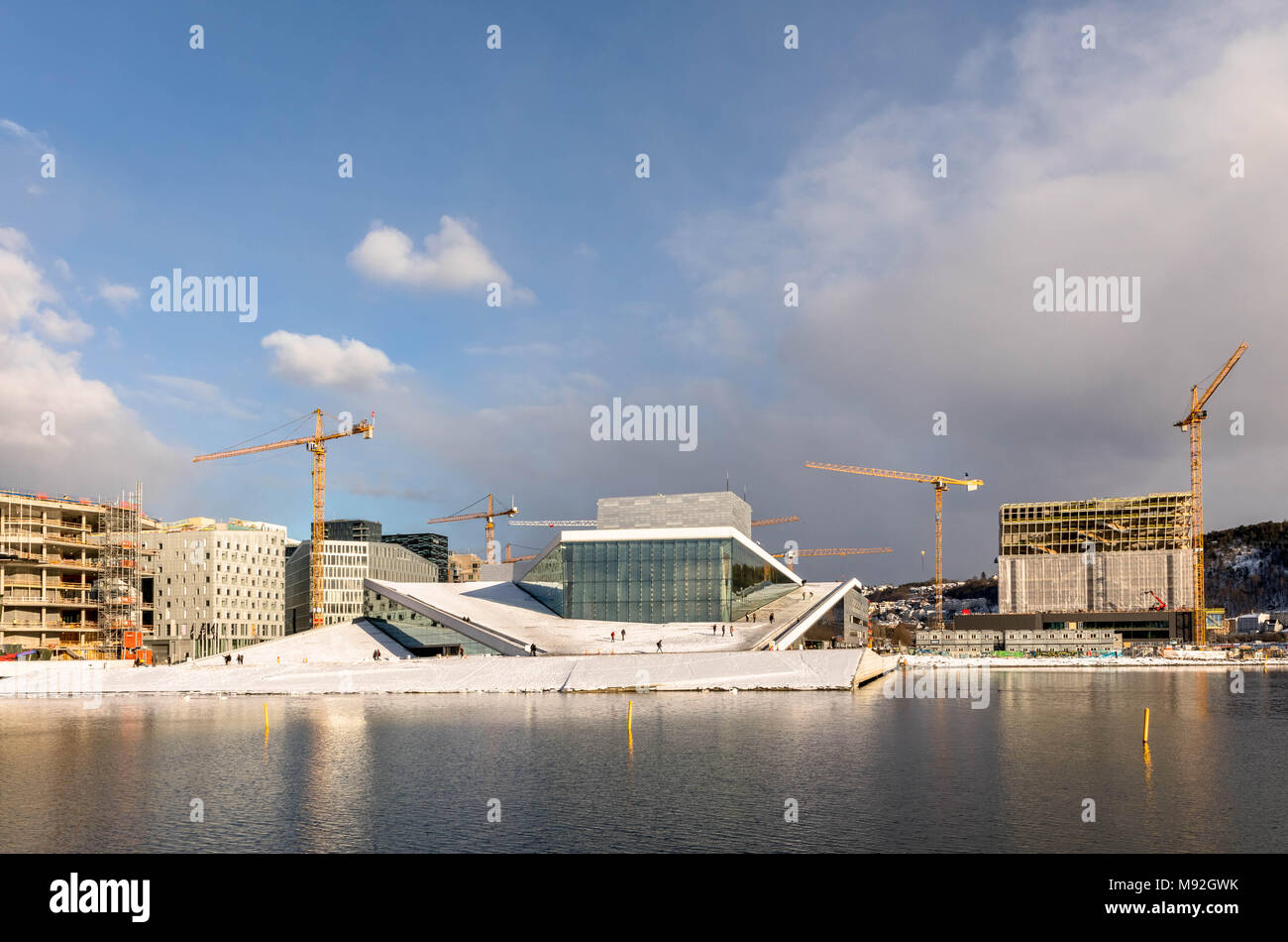 Oslo, Norvège, Mars 2018 : l'Opéra entouré par des grues. En face de la mer, ciel bleu avec des nuages blancs. La neige blanche sur le terrain. Banque D'Images