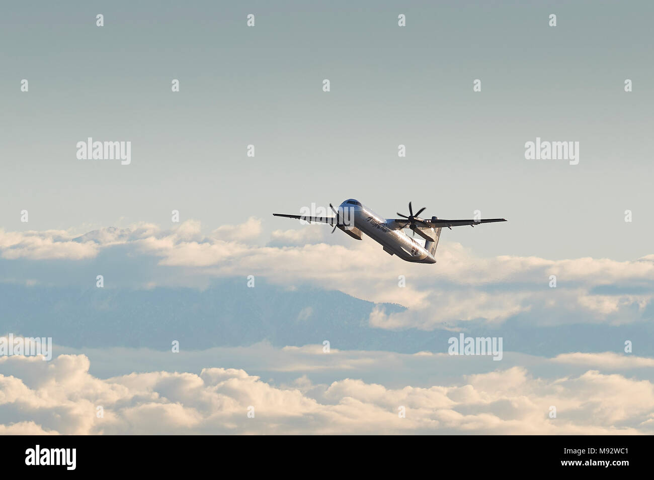 Horizon Air Bombardier Dash 8-Q400 en Alaska Airlines livrée, grimpant de Los Angeles. Nuages sur la ville et des montagnes San Gabriel Banque D'Images