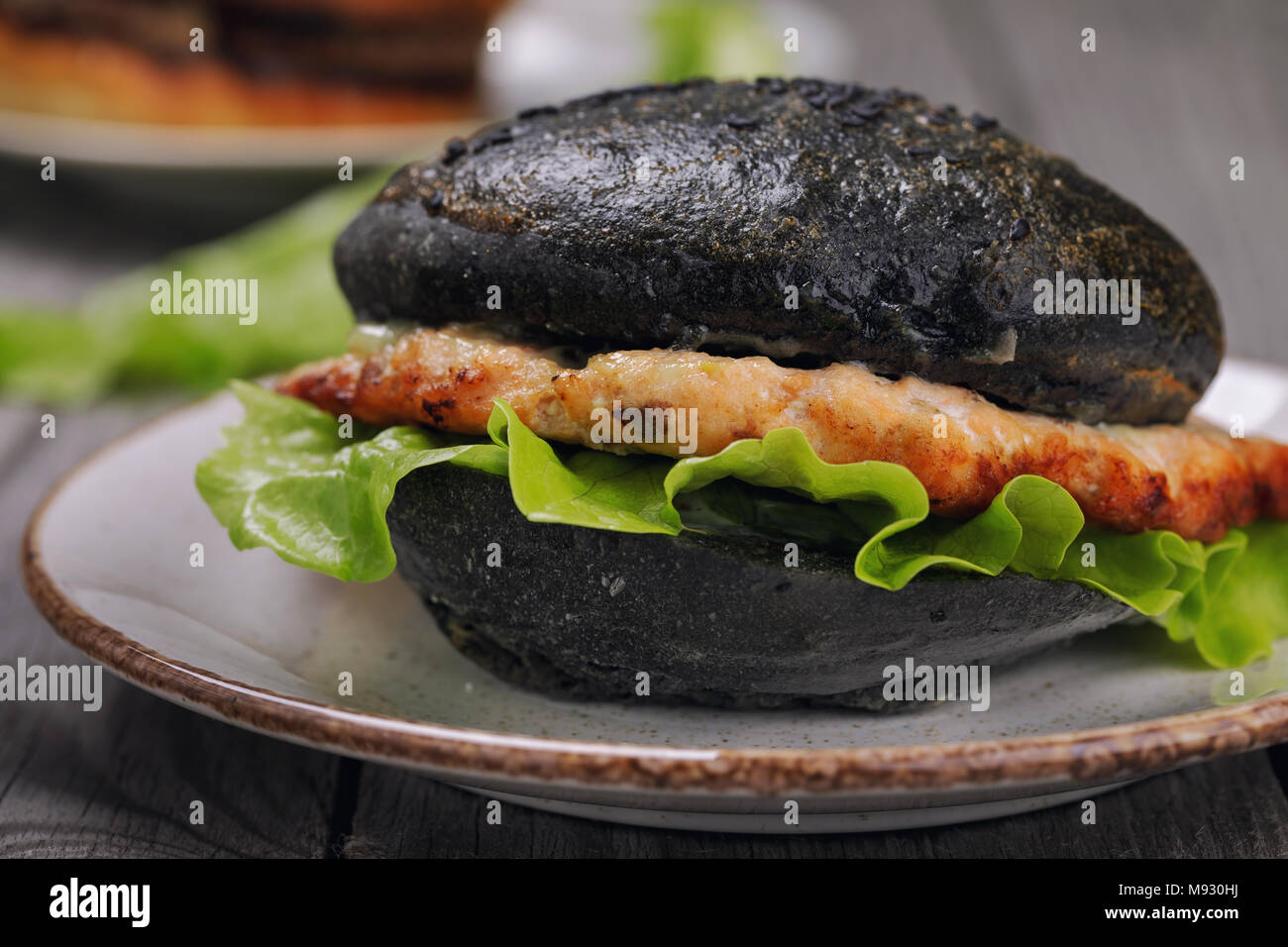 Hamburger fraîchement préparé avec le rouleau de couleur noire, les légumes et le saumon escalope. Gros plan sandwich fait maison Banque D'Images