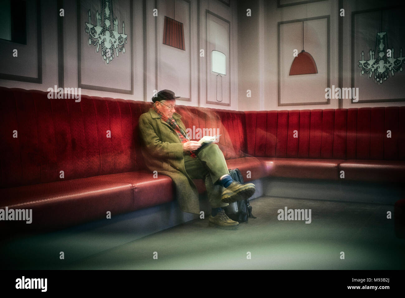 Arty shot d'homme plus âgé en attente d'un train de lire un livre à la salle d'attente de la gare de Crewe Banque D'Images
