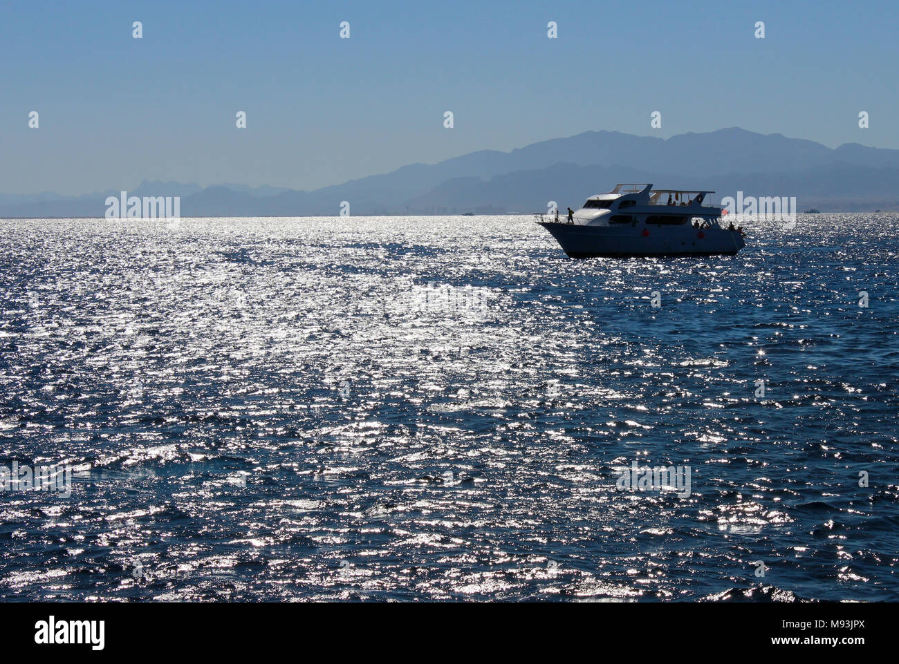 Paysage sur une journée ensoleillée avec vue sur la mer, sur un bateau et les montagnes au loin. Banque D'Images