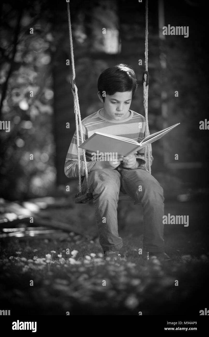 Enfant de lire un livre assis sur une balançoire Banque D'Images