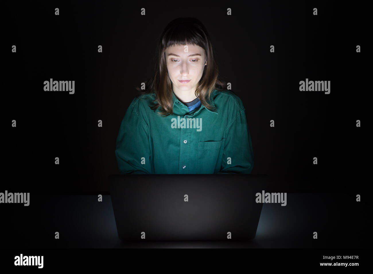 Femme à l'intérieur de l'ordinateur portable à la fin de la soirée. Portrait de jeune femme étudiant ou travailleur assis en face de l'écran de l'ordinateur la nuit et typi Banque D'Images