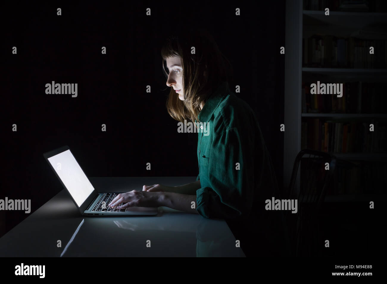 Femme travaille à l'ordinateur portable à la fin de la soirée. Portrait de jeune femme étudiant ou travailleur assis en face de l'écran de l'ordinateur pendant la nuit et en tapant Banque D'Images