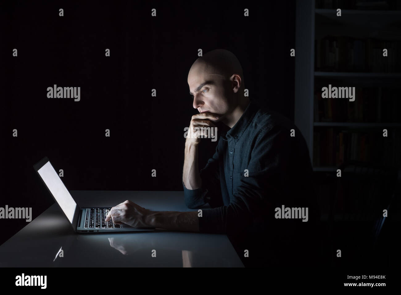 Jeune homme attentif et concentré au pc portable tard dans la soirée. Portrait d'homme sérieux étudiant ou travailleur assis en face de l'écran de l'ordinateur Banque D'Images