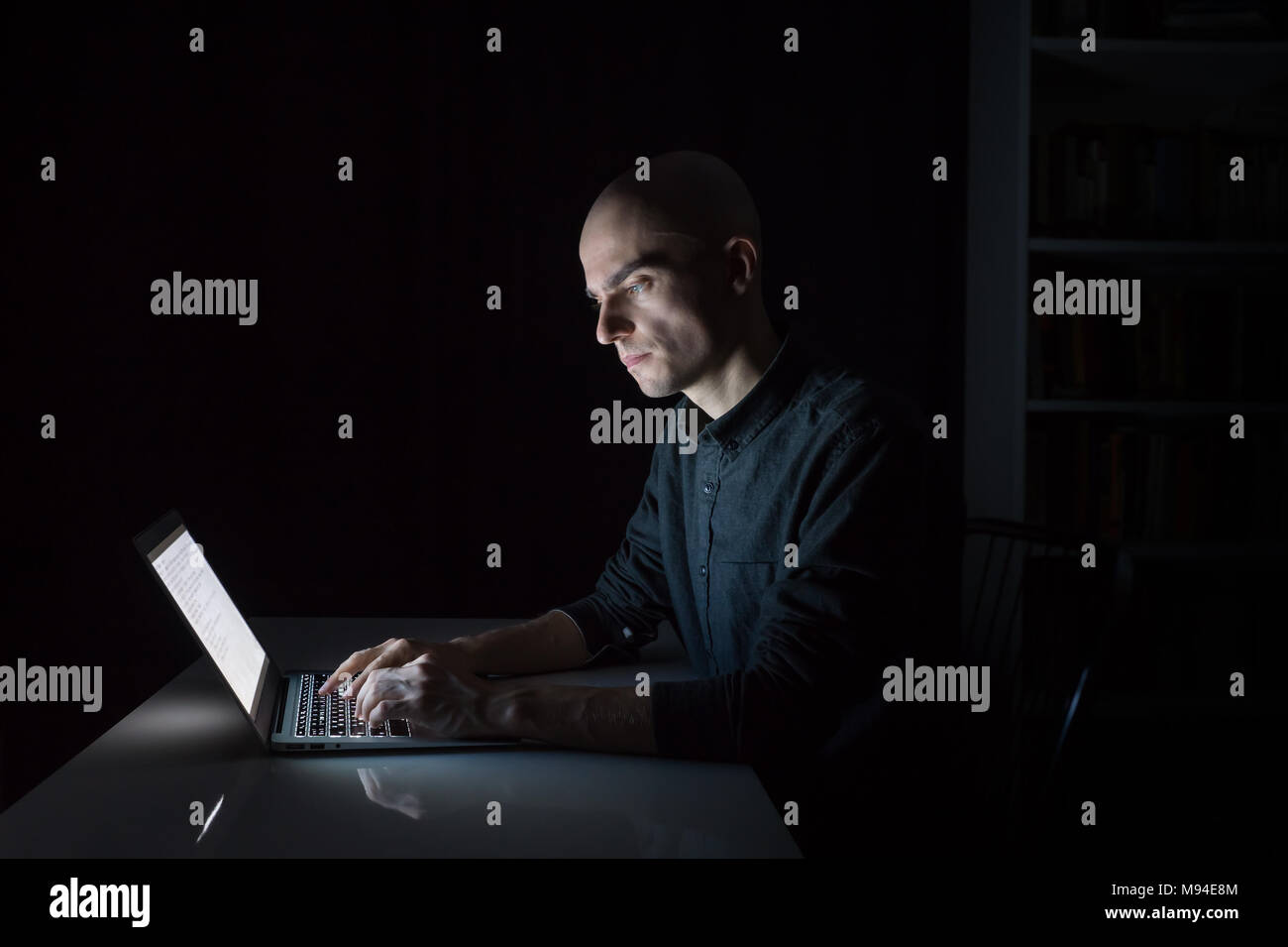 Jeune homme attentif et concentré au pc portable tard dans la soirée. Portrait d'homme sérieux étudiant ou travailleur assis en face de l'écran de l'ordinateur Banque D'Images