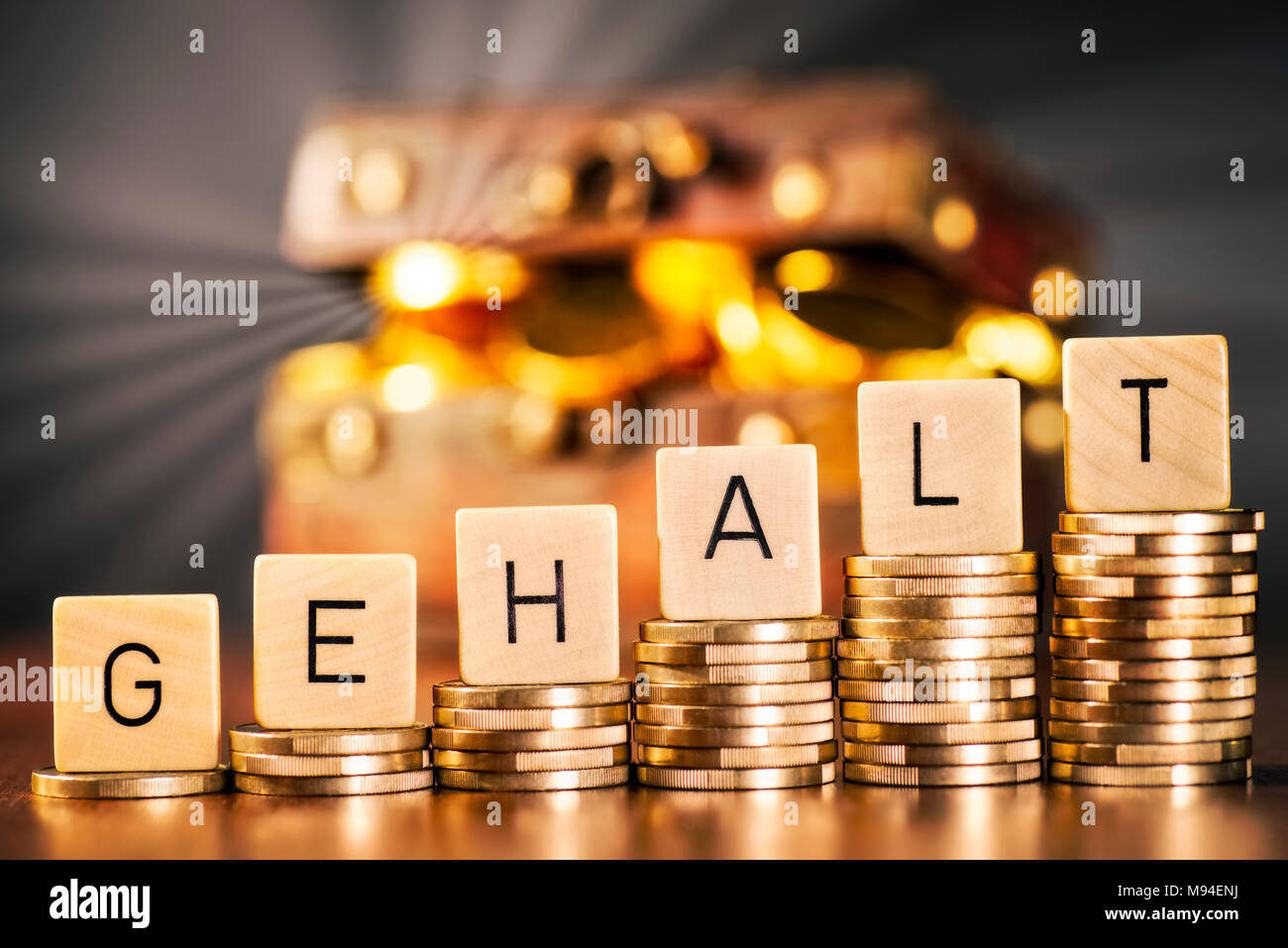 Le mot allemand 'Gehalt' pour les salaires sur l'augmentation des piles avec coins en face d'une poitrine avec de l'argent dans l'arrière-plan. Banque D'Images