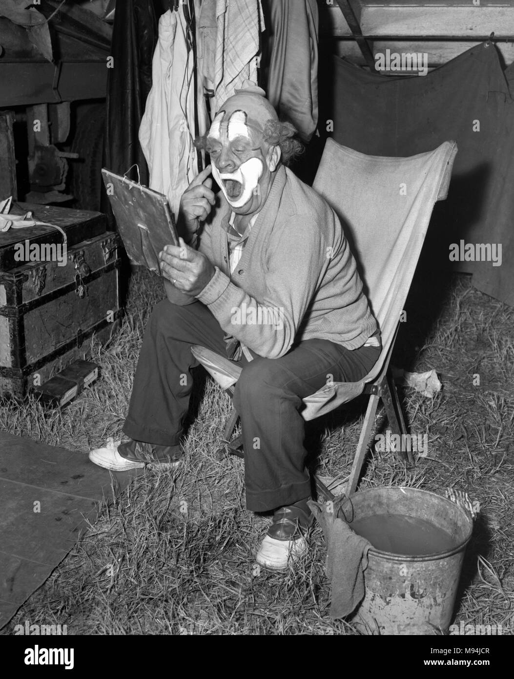 Un clown s'applique la peinture de graisse avant un spectacle, ca. 1953. Banque D'Images