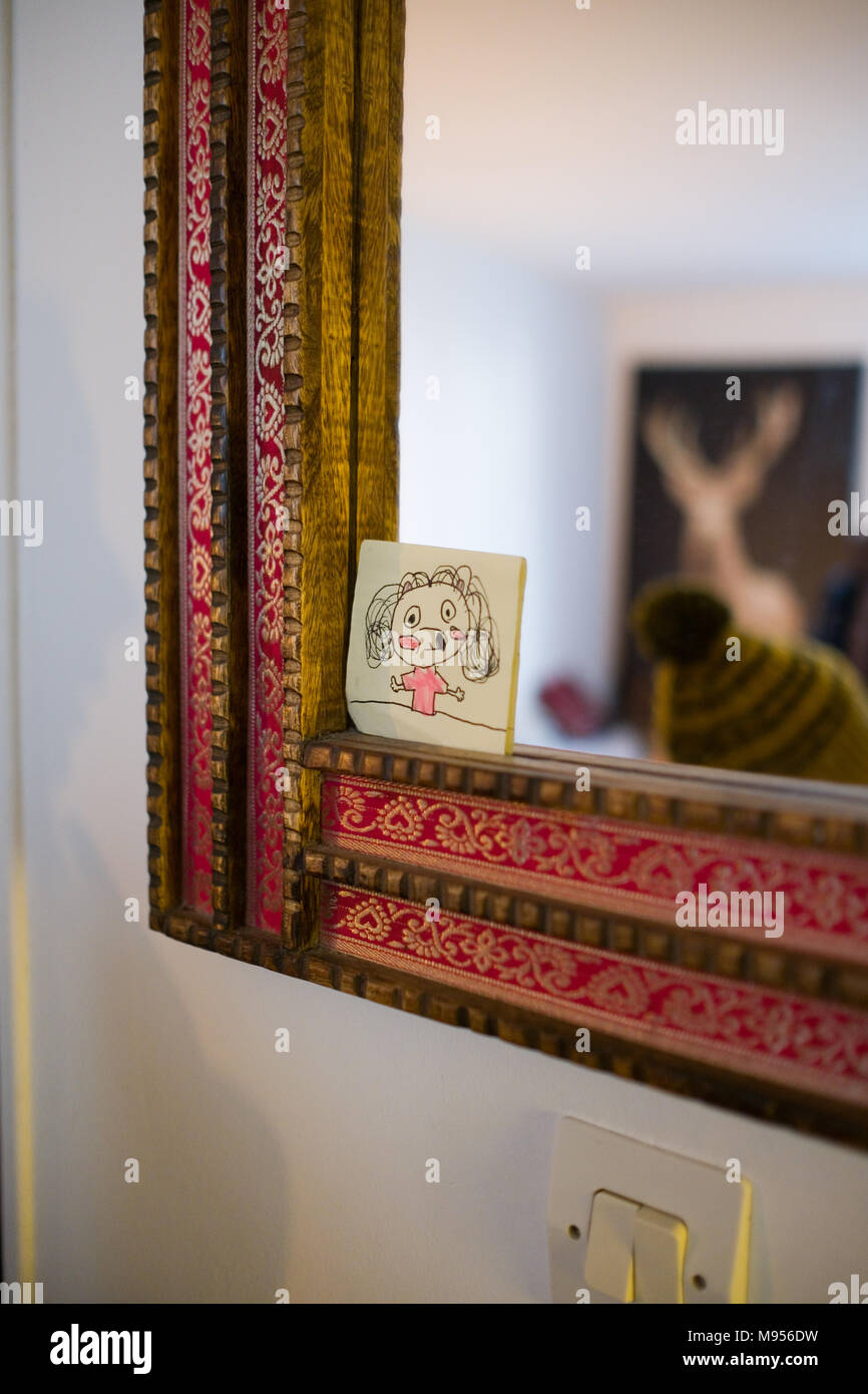 Un croquis de l'enfant d'une fille, c'est coincé dans le cadre d'un miroir dans un environnement familial. Dans la réflexion que nous voyons un hiver bobble hat et un flou poster Banque D'Images