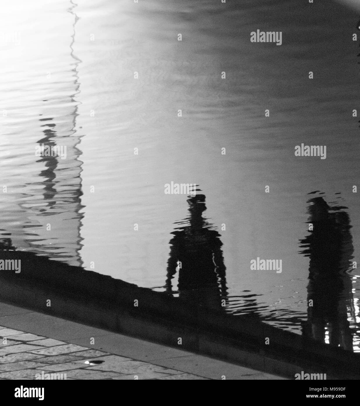 Réflexions de deux personnes sur la surface ondulée d'un canal dans la ville de Milan, Italie Banque D'Images