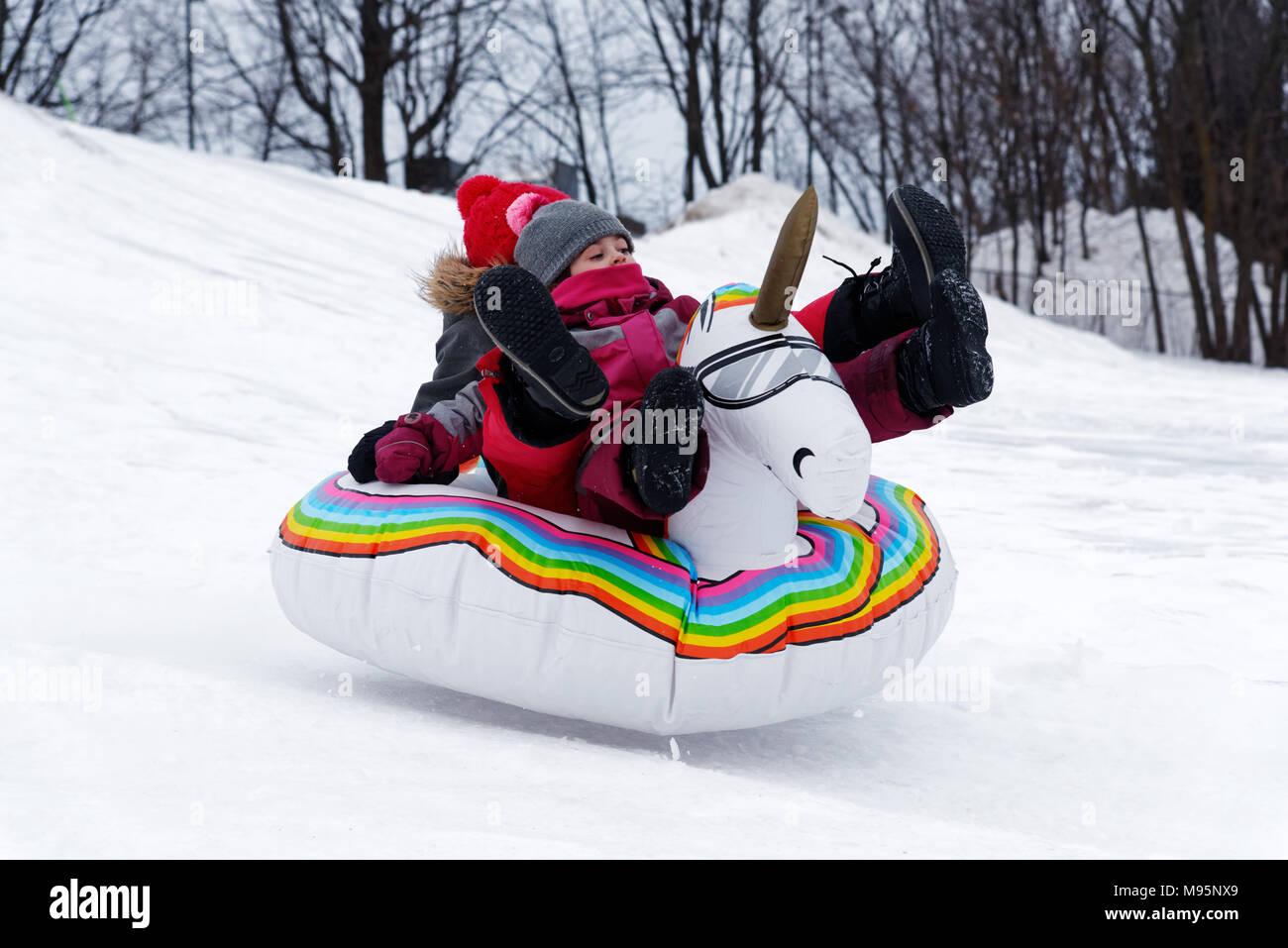 Deux fille glisser dans la neige sur un blow-up unicorn, Québec Canada Banque D'Images