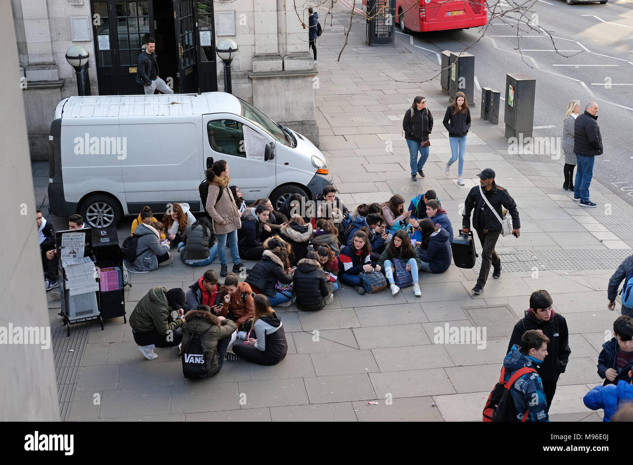 Un grand groupe d'élèves assis sur le trottoir à Londres. Banque D'Images