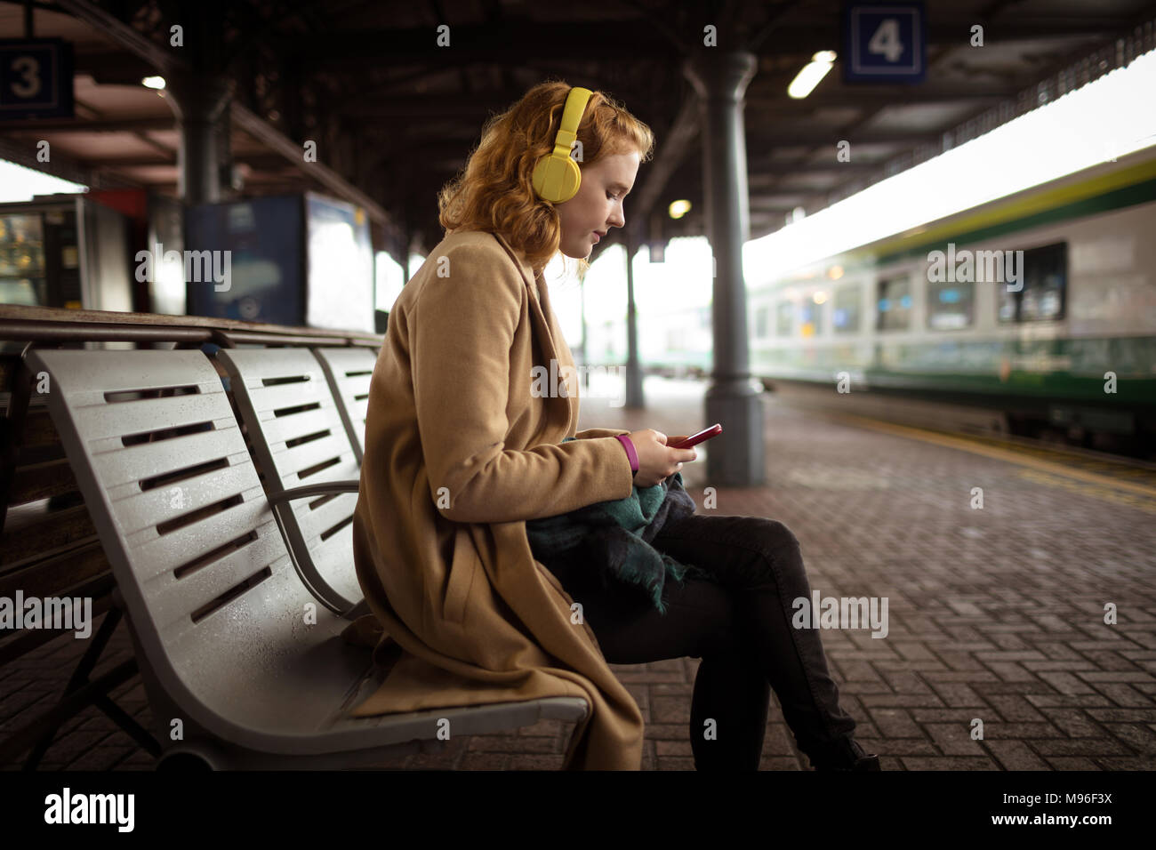 Belle jeune femme énumérant la musique tout en utilisant son téléphone portable Banque D'Images