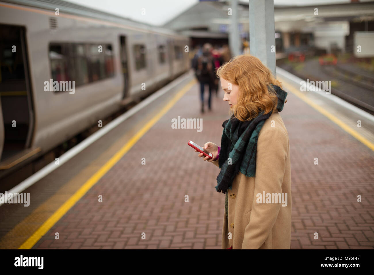 Jeune femme debout sur un quai de gare en utilisant son téléphone portable Banque D'Images