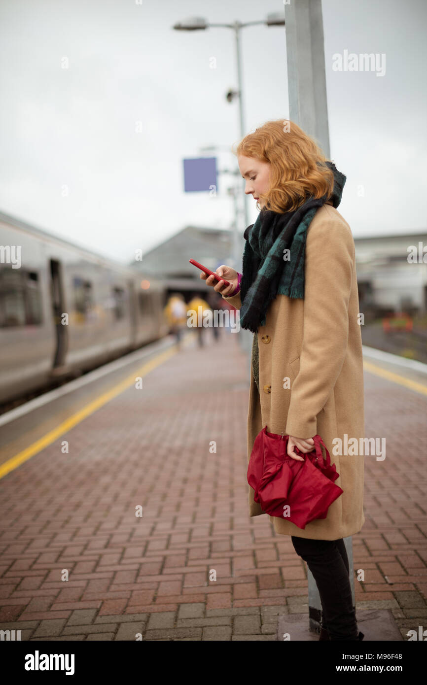 Jeune femme debout sur un quai de gare en utilisant son téléphone portable Banque D'Images