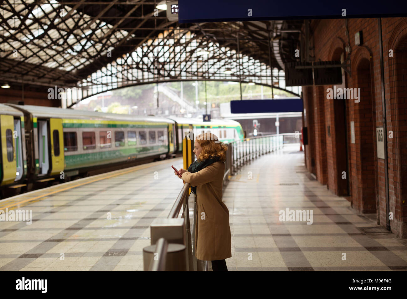 Jeune femme debout sur un quai de gare en utilisant son téléphone portable Banque D'Images