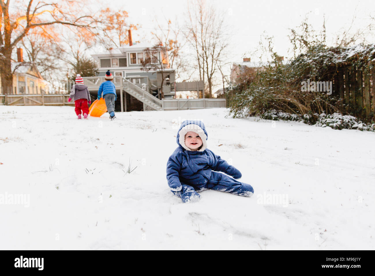 Girl smiling sitting dans la neige avec les autres enfants jouant dans l'arrière-plan Banque D'Images