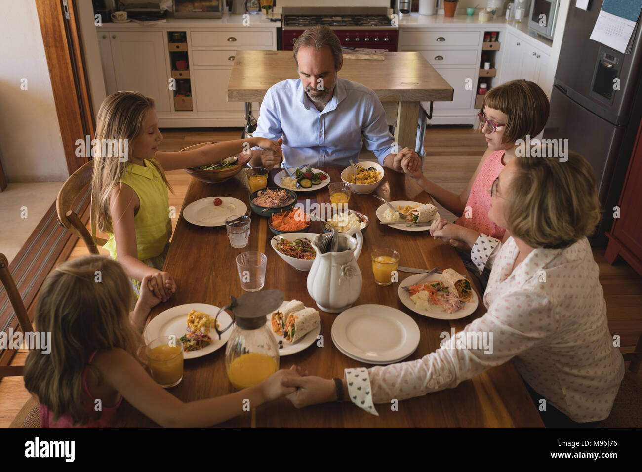 Famille prier ensemble avant d'avoir le déjeuner dans la cuisine Banque D'Images