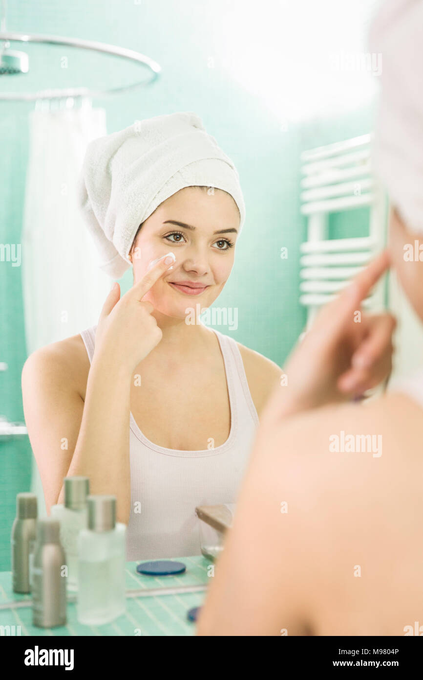 Young woman applying facial hydratant au miroir dans salle de bains Banque D'Images