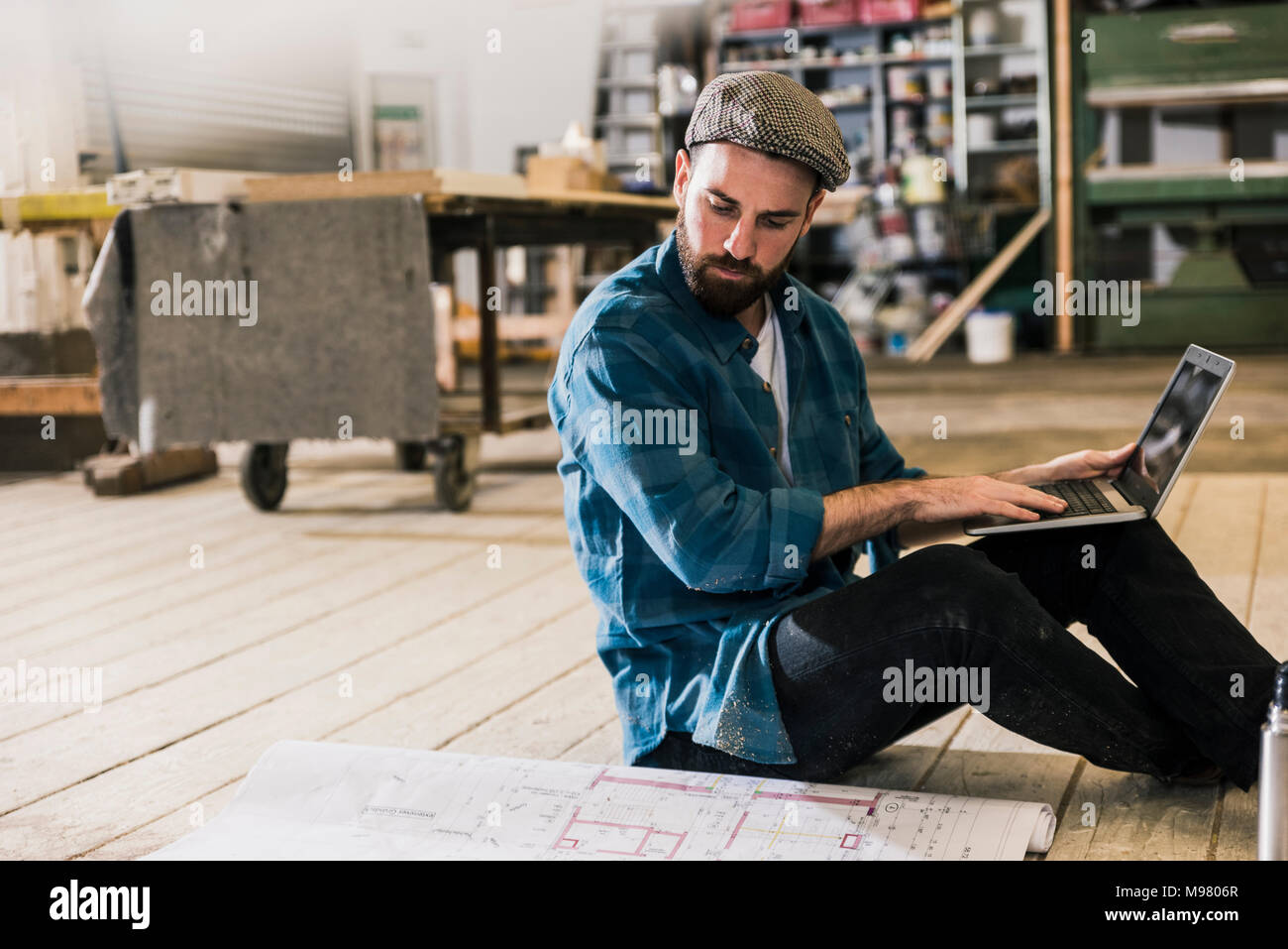 Homme avec portable assis sur le plancher à la recherche au plan de construction Banque D'Images