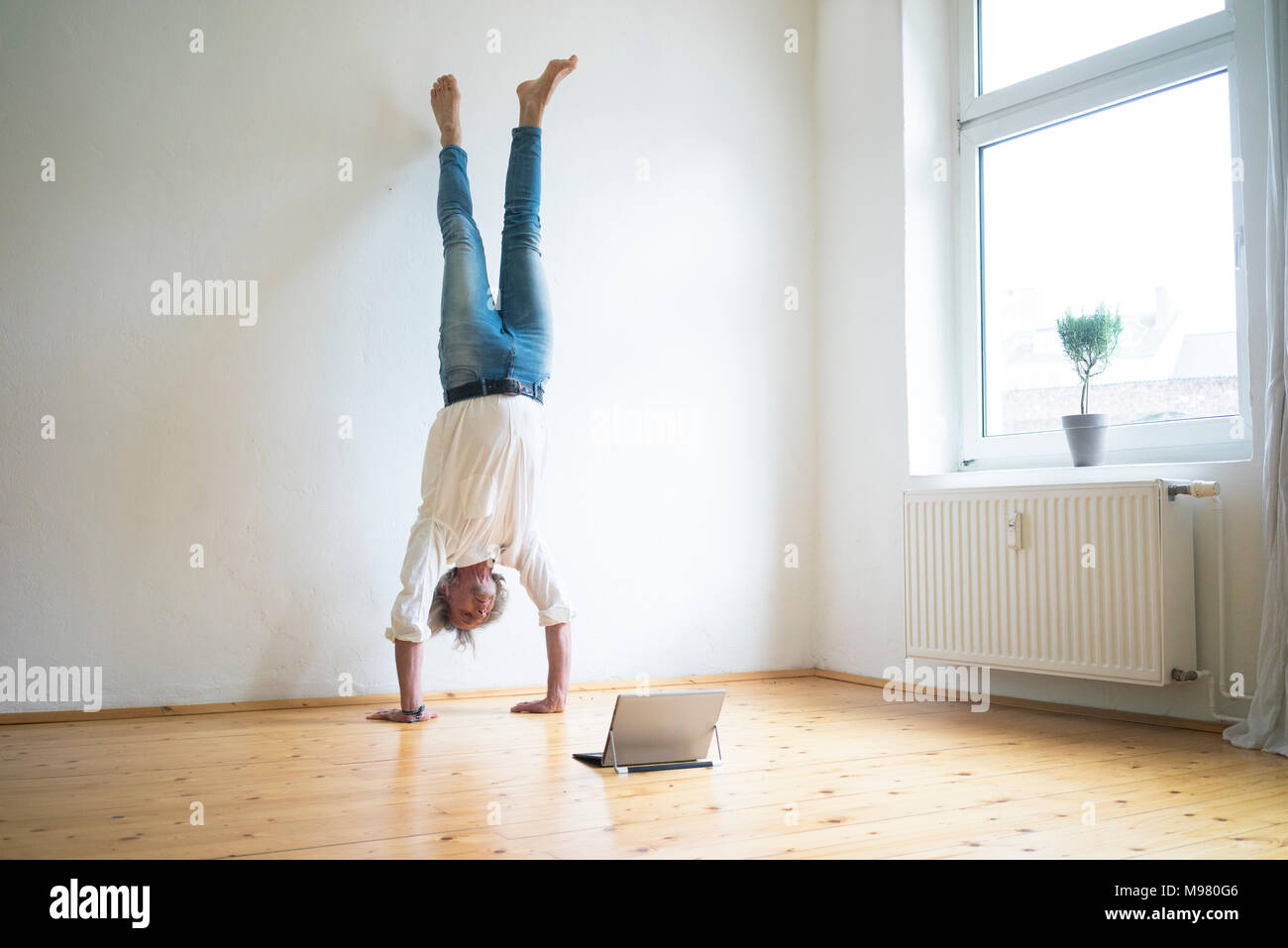 Man doing a handstand in empty room looking at tablet Banque D'Images