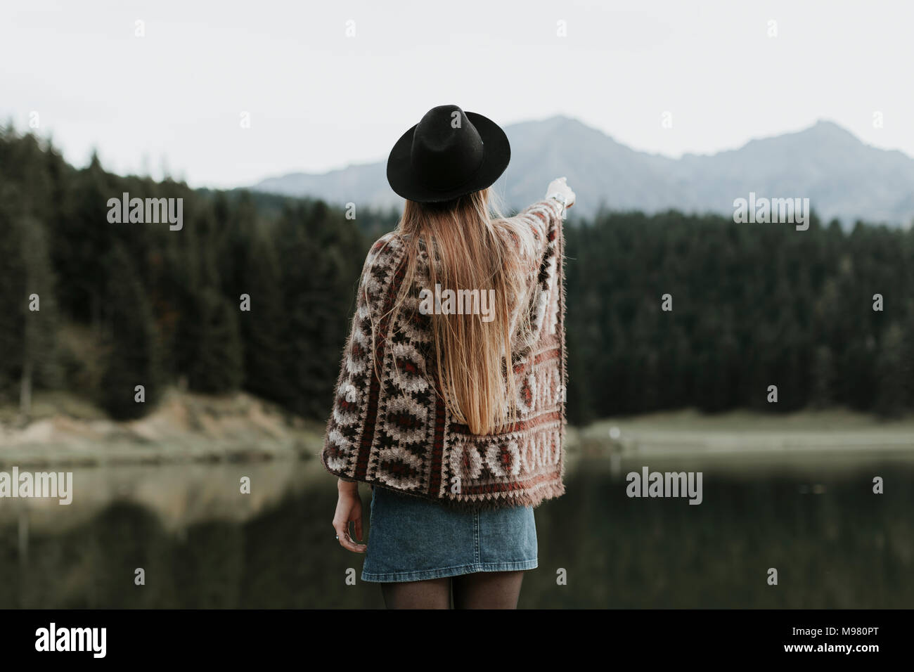 Vue arrière de la mode jeune femme portant chapeau et poncho standing in front of a lake Banque D'Images