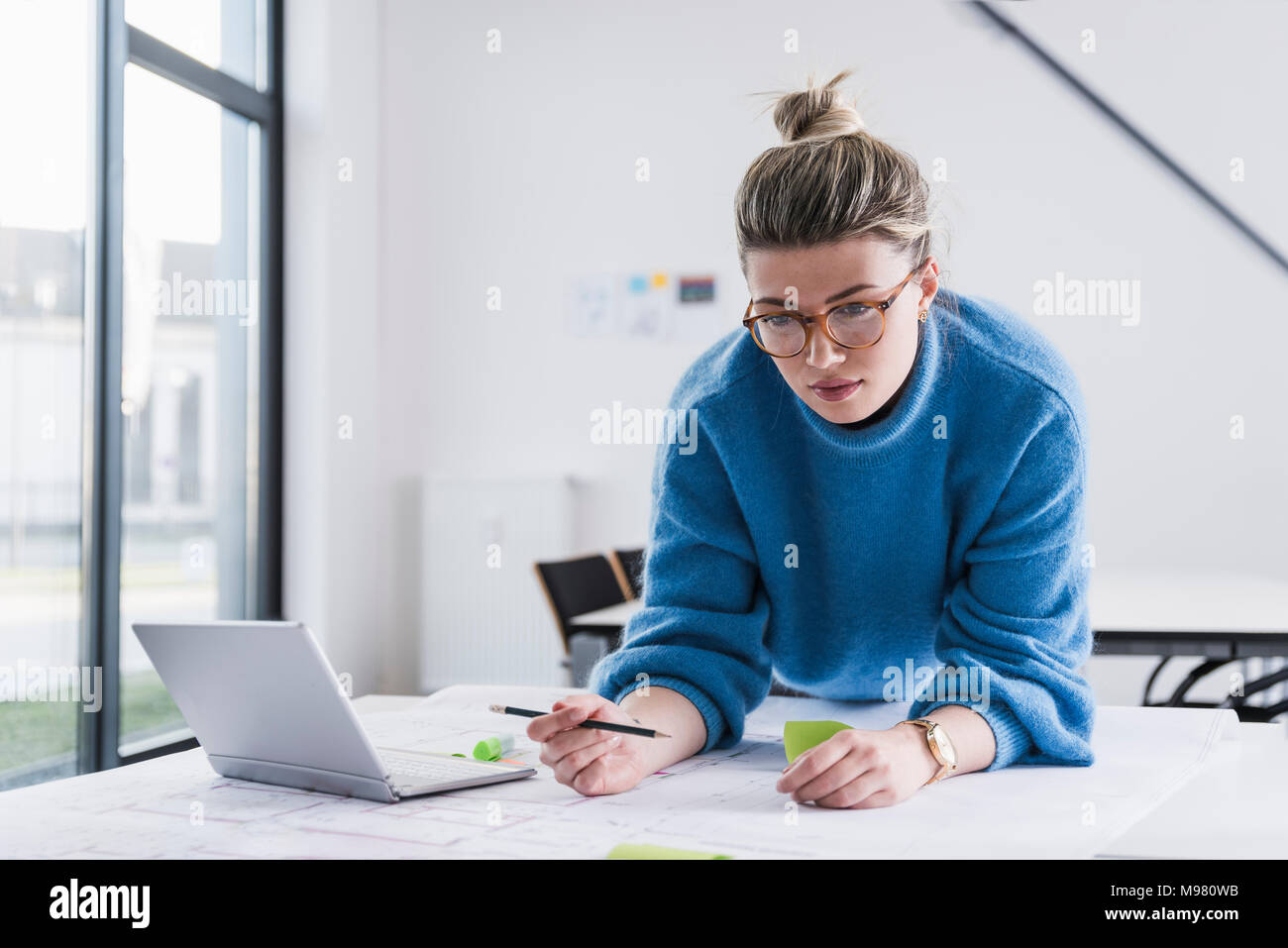 Young woman with laptop travaillant sur plan at desk in office Banque D'Images