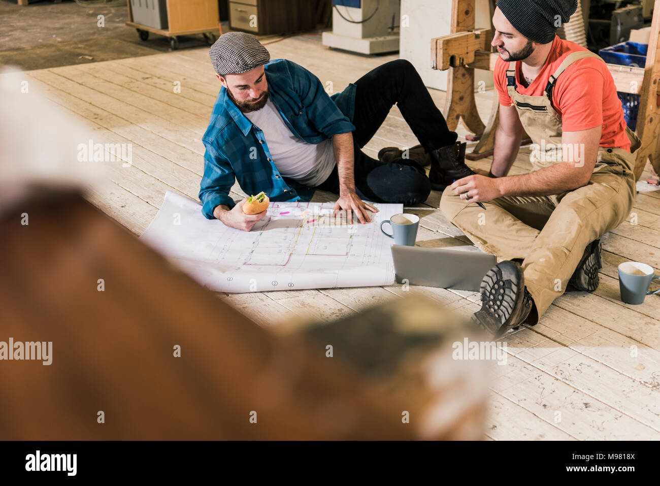 Deux hommes avec un ordinateur portable à la recherche au plan de la construction sur le sol Banque D'Images