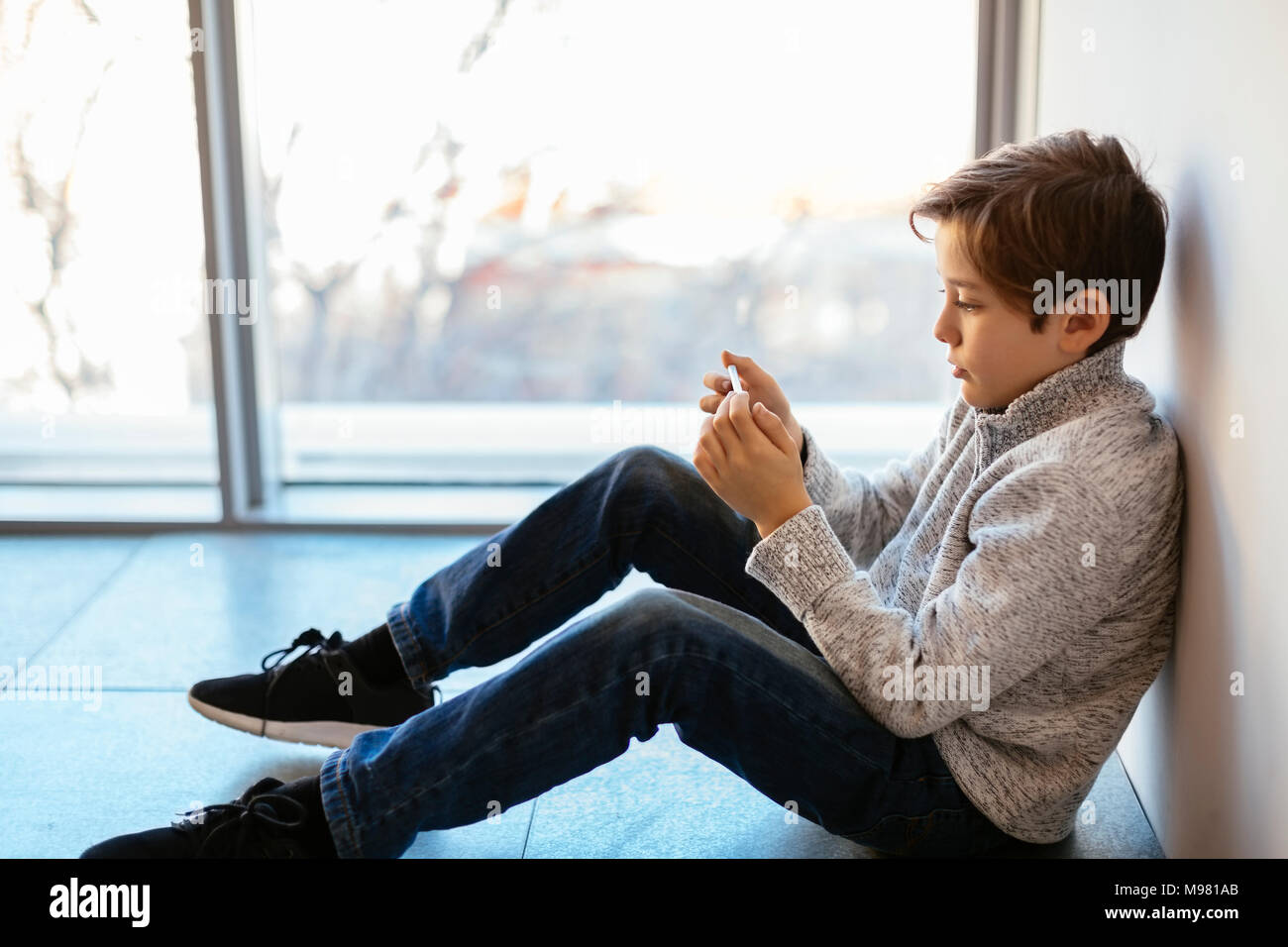 Boy sitting on floor looking at cell phone Banque D'Images