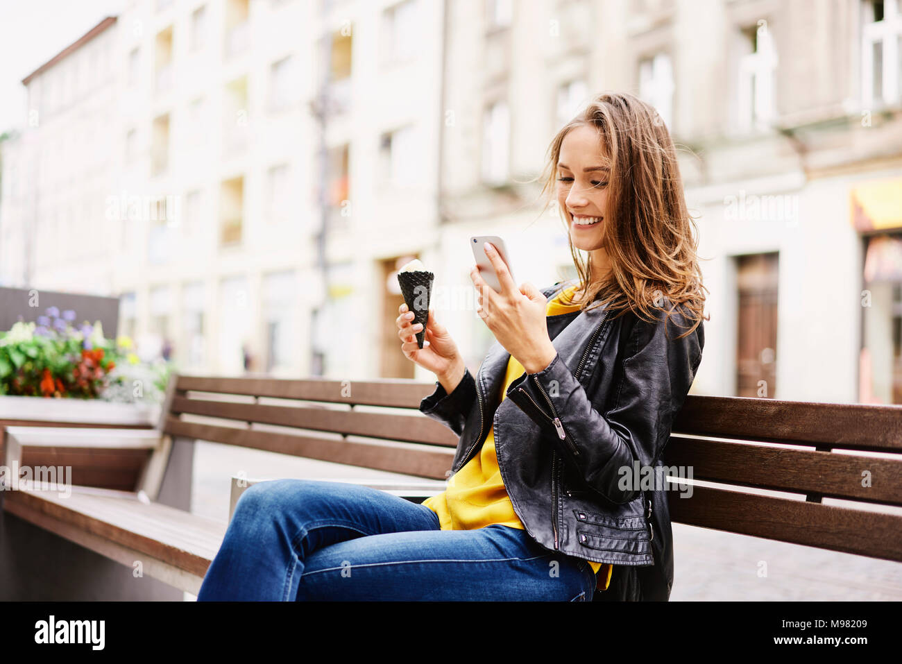 Portrait of happy woman sitting on bench with ice cream cone looking at cell phone Banque D'Images