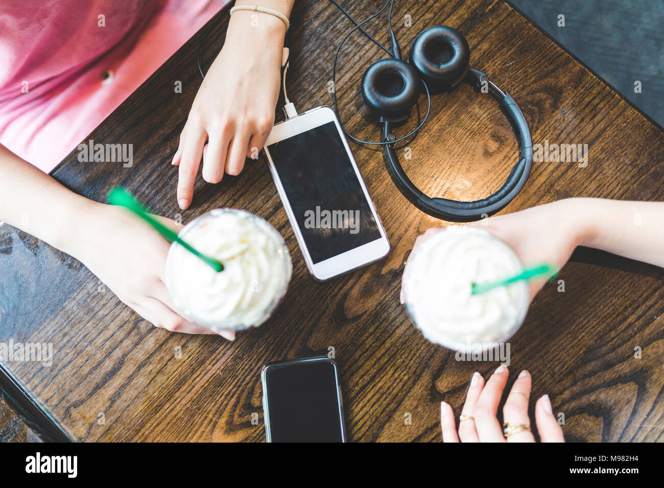 Deux femmes à table avec des milkshakes, des téléphones cellulaires et casque Banque D'Images