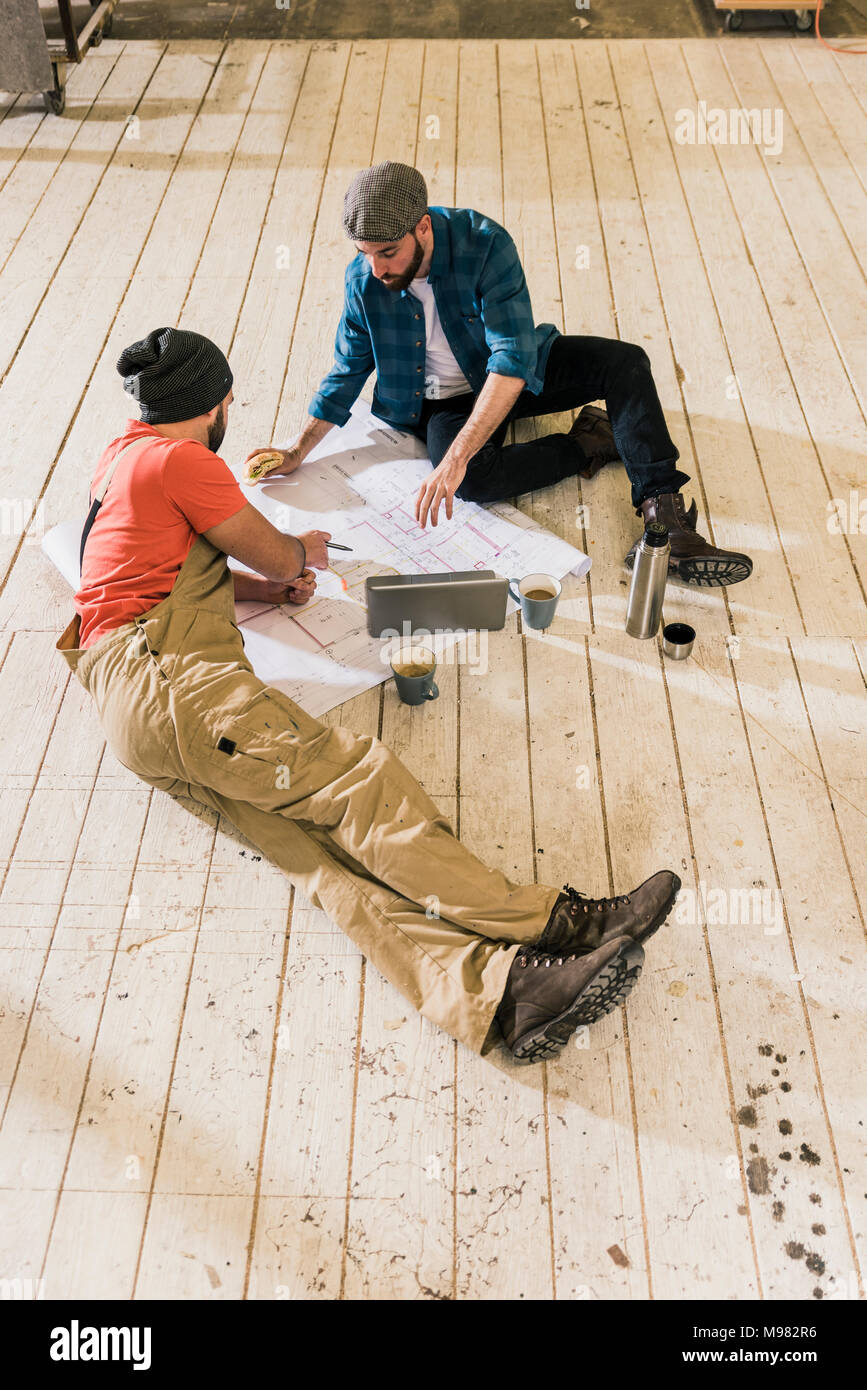 Deux hommes avec un ordinateur portable à la recherche au plan de la construction sur le sol Banque D'Images
